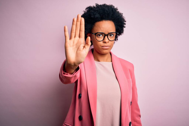 Mladá krásná afro americká obchodnice s kudrnatými vlasy v růžové bundě přestává zpívat dlaní ruky. Varovný výraz s negativním a vážným gestem na tváři. - Fotografie, Obrázek