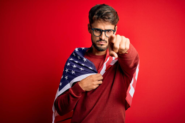 Young man wearing glasses and United States of America flag over isolated red background pointing with finger to the camera and to you, hand sign, positive and confident gesture from the front - Fotó, kép