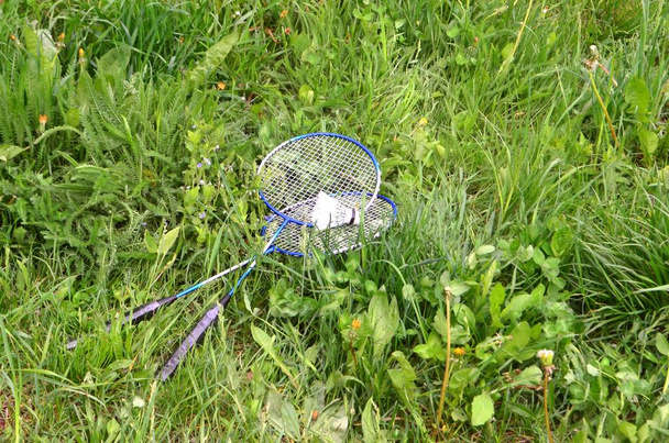 Ended games and rackets along with a shuttlecock, thrown into the spring, green grass. - Photo, Image