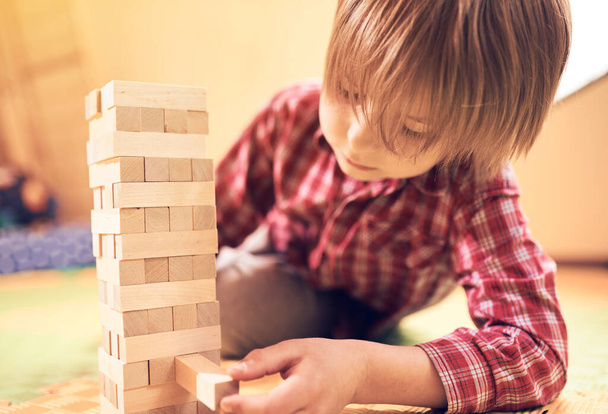 Preschool cute boy playing in a table game with wooden blocks at home. Players take turns removing one block at a time from a tower. Each block removed is then placed on top of the tower. - Фото, зображення