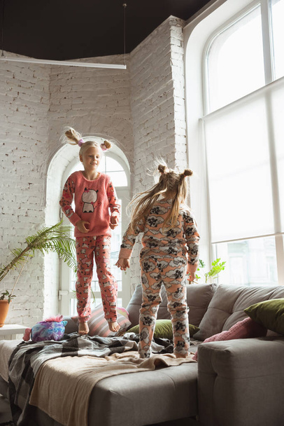 Quiet little girls playing in a bedroom in cute pajamas, home style and comfort, laughting and fighting pillows, jumping high - Foto, immagini
