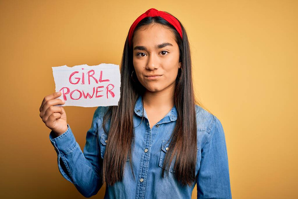 Junge schöne asiatische Frau trägt Diadema hält Banner mit Girl Power Botschaft mit einem selbstbewussten Gesichtsausdruck auf intelligentem Gesichtsdenken ernst - Foto, Bild