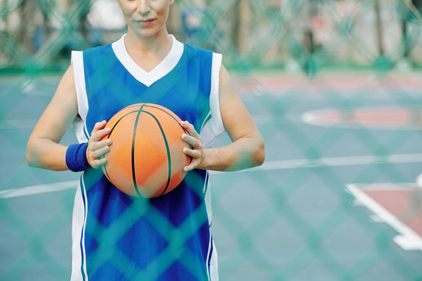 Imagen recortada del jugador de baloncesto femenino de pie en la cancha al aire libre y sosteniendo la pelota - Foto, Imagen