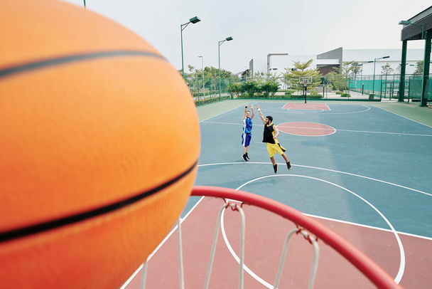 Человек бросает и получает мяч в корзину во время игры в баскетбол на открытом воздухе - Фото, изображение