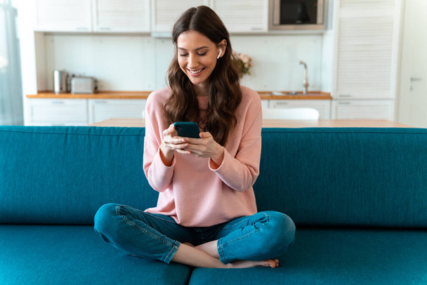 Image of a positive happy beautiful young woman sit indoors at home using mobile phone on sofa. - Φωτογραφία, εικόνα