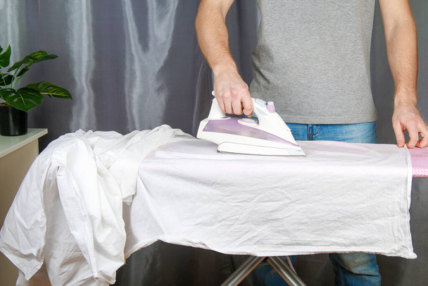 A man strokes linen with an black electric iron on an ironing board. Household. - Photo, image