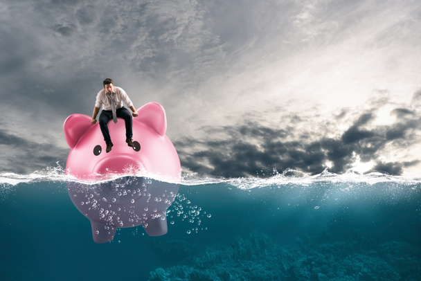 Business man in financial trouble sails on piggy bank in bad waters due to the crisis - Photo, Image