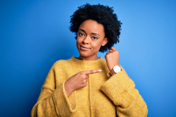 Young beautiful African American afro woman with curly hair wearing yellow casual sweater In hurry pointing to watch time, impatience, looking at the camera with relaxed expression - Fotoğraf, Görsel