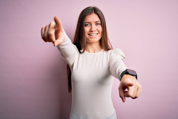 Young beautiful woman with blue eyes wearing casual white t-shirt over pink background pointing to you and the camera with fingers, smiling positive and cheerful - Photo, Image