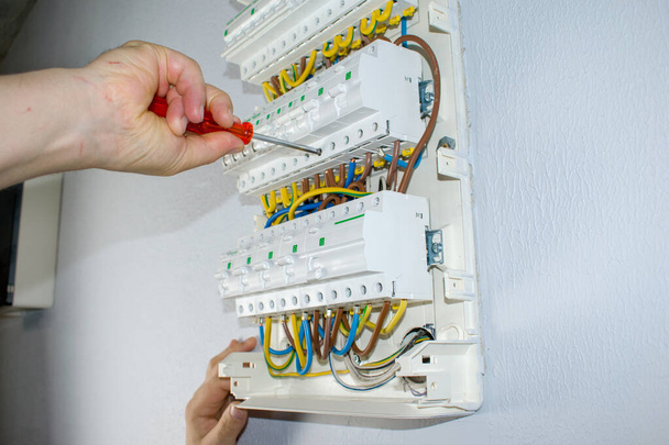 Um eletricista masculino trabalha em um quadro com um cabo de conexão elétrica, fusíveis. Conecta o equipamento com ferramentas, o conceito de trabalho complexo
. - Foto, Imagem