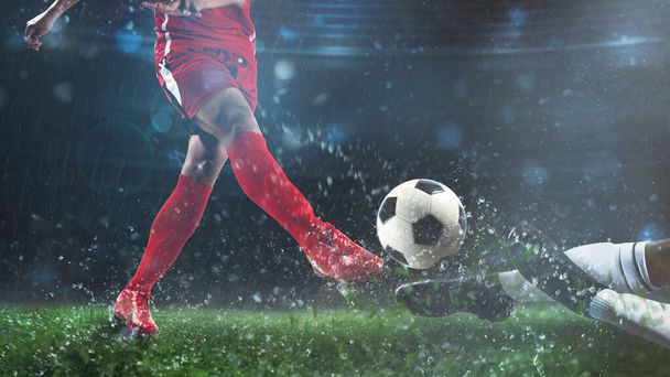Escena de fútbol en el partido de noche con el jugador en un uniforme rojo pateando la pelota y oponente en tackle para defender
 - Foto, imagen