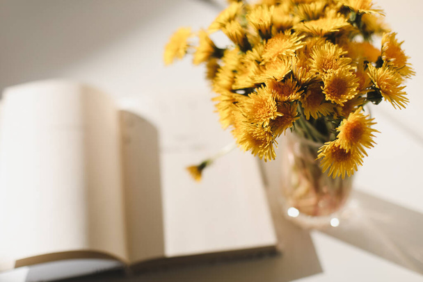 A book and a bunch of yellow dandelions.  Still life with wild flowers.  Play of light and shadow. Summer flowers - Photo, image
