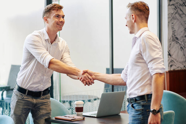 Excited smiling young entrepreneur shaking hand of business partner he meeting in cafe - Photo, Image