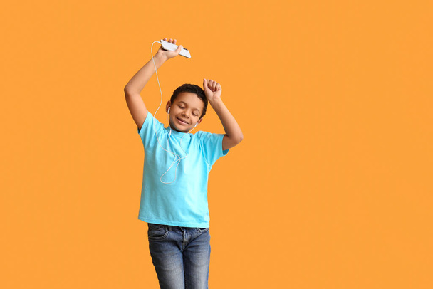 Little African-American boy listening to music and dancing against color background - Φωτογραφία, εικόνα