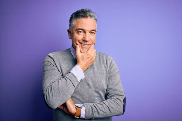 Middle age handsome grey-haired man wearing elegant sweater over purple background looking confident at the camera smiling with crossed arms and hand raised on chin. Thinking positive. - Fotoğraf, Görsel
