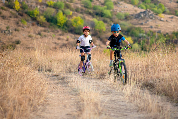 fröhliche Mädchen und Jungen, die sich an einem schönen Herbsttag mit dem Fahrrad im Herbstpark vergnügen. Aktive Kinder mit Fahrradhelm - Foto, Bild