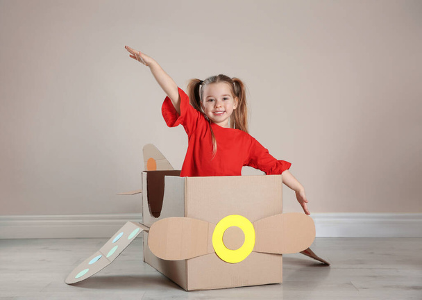 Cute little child playing with cardboard plane near beige wall - Фото, изображение