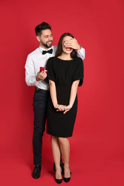 Man with engagement ring making marriage proposal to girlfriend on red background - Foto, Imagem