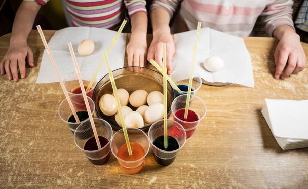 Close up video of hands of children using dye and painting on white boiled eggs while preparing for Easter - Foto, imagen