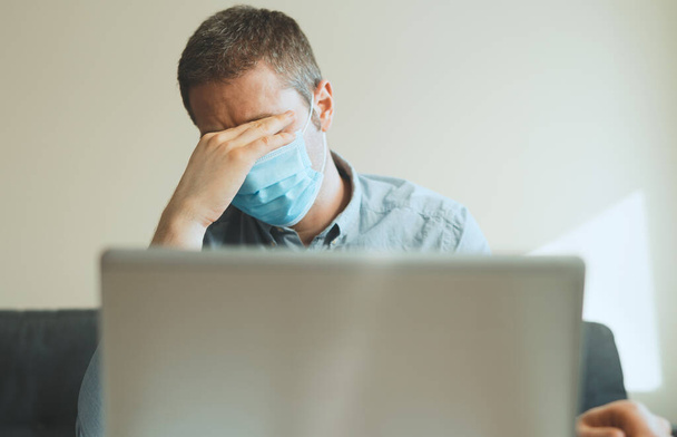 Hombre cansado en máscara médica trabajando en la computadora en el interior
. - Foto, Imagen