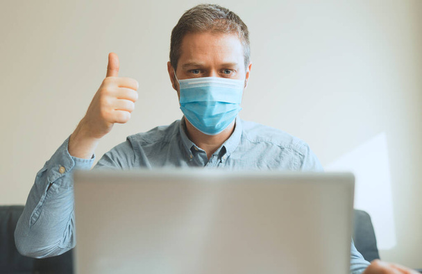 Man in medical mask showing thumbs up via video calling. - Foto, imagen