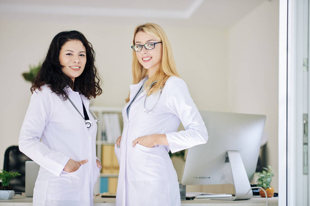 Retrato de jóvenes y alegres trabajadoras médicas en batas blancas de laboratorio sonriendo a la cámara
 - Foto, Imagen