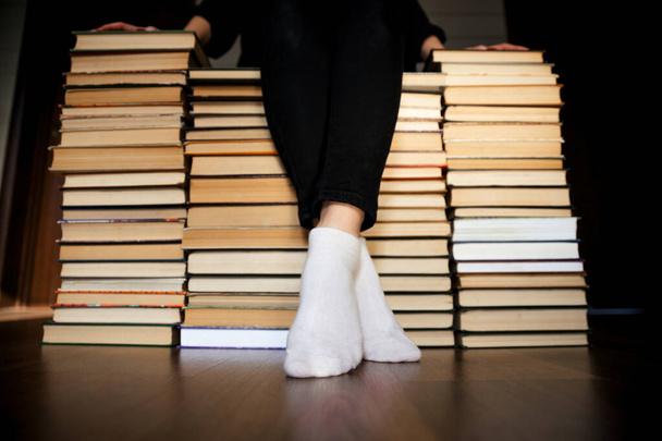 Nainen istuu kirjaarkistojen vuorella. Jalat valkoisilla sukilla
 - Valokuva, kuva
