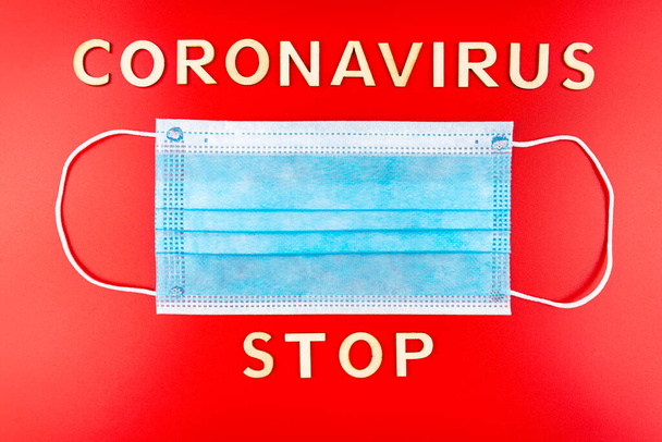 Masque chirurgical jetable bleu, isolé sur un fond rouge avec l'inscription en bois "stop coronavirus
". - Photo, image