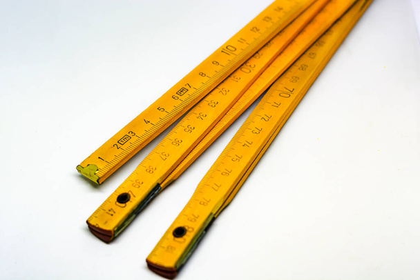 Medidor plegable de madera amarillo con extremos de latón aislados sobre un fondo blanco. Totalmente extendido mide 2 metros. Instrumento de medida utilizado en la industria de la construcción
 - Foto, imagen