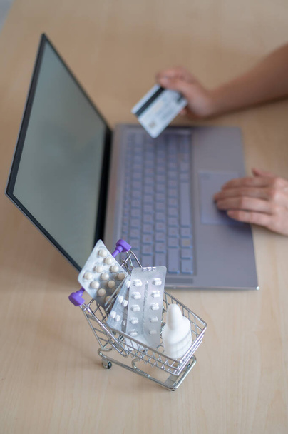 Online pharmacy concept. A woman holds a debit card in her hands and buys pills online. A girl makes an online purchase of medicines with home delivery on a laptop. - Foto, Imagem