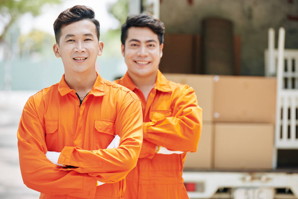 Usmívající se asijské stěhovací pracovníci stojící před kamion naložený lepenkovými krabicemi - Fotografie, Obrázek