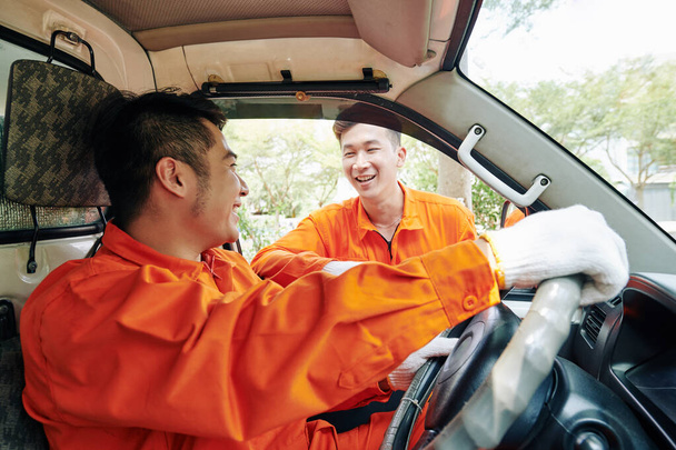 Uśmiechnięci wietnamscy kierowcy usług dostawczych w mundurach odbywający pogawędkę przed rozpoczęciem pracy - Zdjęcie, obraz