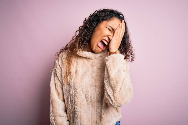 Young beautiful woman with curly hair wearing casual sweater standing over pink background Yawning tired covering half face, eye and mouth with hand. Face hurts in pain. - Fotó, kép