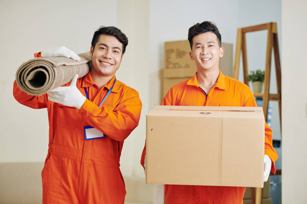 Trabalhadores de serviços móveis positivos transportando tapete laminado e caixa de papelão - Foto, Imagem