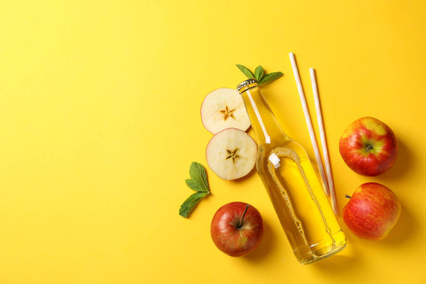 Komposition mit Apfelwein, Äpfeln und Strohhalmen auf gelbem Hintergrund - Foto, Bild