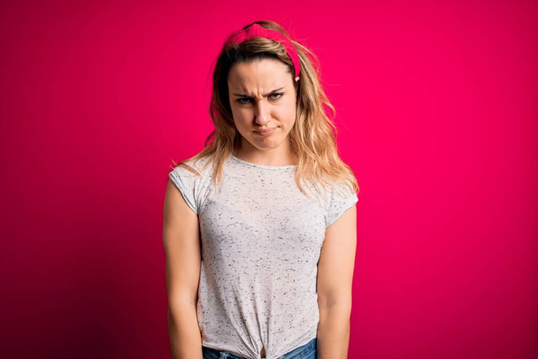 Junge schöne blonde Frau in lässigem T-Shirt vor isoliertem rosa Hintergrund skeptisch und nervös und runzelt die Stirn wegen des Problems. Negative Person. - Foto, Bild