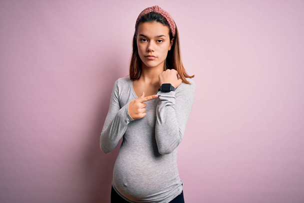 Joven hermosa adolescente embarazada esperando bebé sobre fondo rosa aislado En prisa apuntando a ver el tiempo, la impaciencia, mirando a la cámara con expresión relajada
 - Foto, imagen