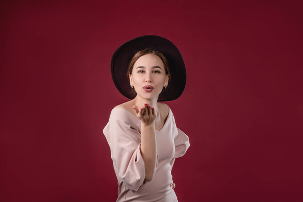 Portrait of a beautiful girl who straightens a hat on a red background. The concept of beauty and youth - Foto, imagen