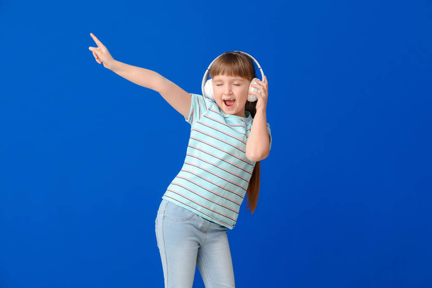Cute little girl dancing and listening to music against color background - Zdjęcie, obraz