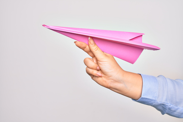 Main de caucasienne jeune femme tenant avion en papier sur fond blanc isolé - Photo, image