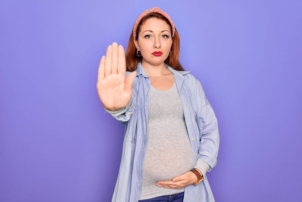 Young beautiful redhead pregnant woman expecting baby over isolated purple background doing stop sing with palm of the hand. Warning expression with negative and serious gesture on the face. - Foto, immagini