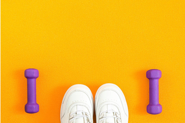 Cipők és súlyzók a narancssárga fitneszszőnyeg hátterén. Lapos kompozíció. A sport, a fitnesz, az egészséges életmód fogalma. Első látásra. Fénymásolási hely. - Fotó, kép