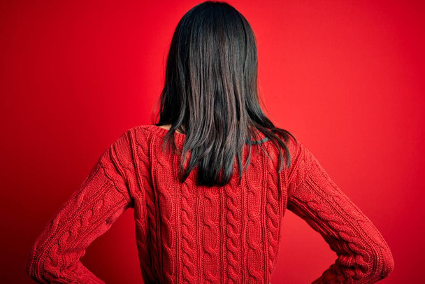 Giovane donna bruna con gli occhi blu che indossa maglione casual su sfondo rosso isolato in piedi all'indietro guardando con le braccia sul corpo
 - Foto, immagini