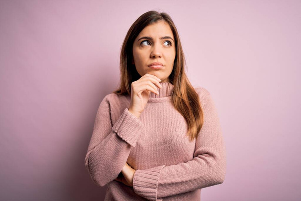 Beautiful young woman wearing turtleneck sweater over pink isolated background with hand on chin thinking about question, pensive expression. Smiling with thoughtful face. Doubt concept. - Foto, afbeelding
