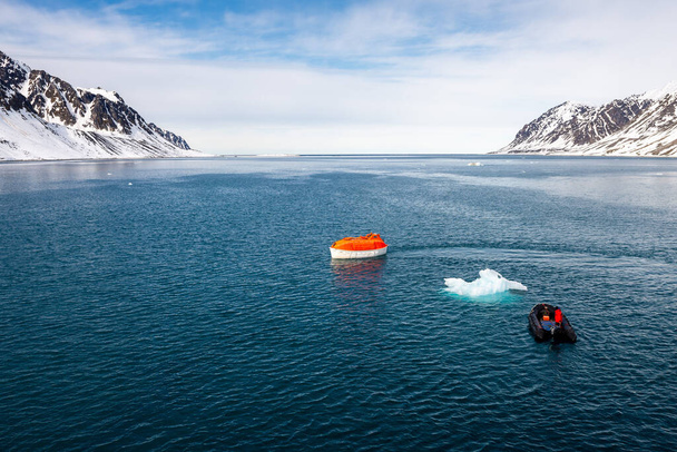 Maniobrando bote salvavidas naranja en aguas del Ártico, Svalbard. Abandonen el simulacro. Entrenamiento en botes salvavidas. Hombre sobre tabla taladro
. - Foto, Imagen