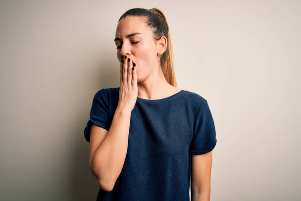 Young beautiful blonde woman with blue eyes wearing casual t-shirt over white background bored yawning tired covering mouth with hand. Restless and sleepiness.  - Photo, Image