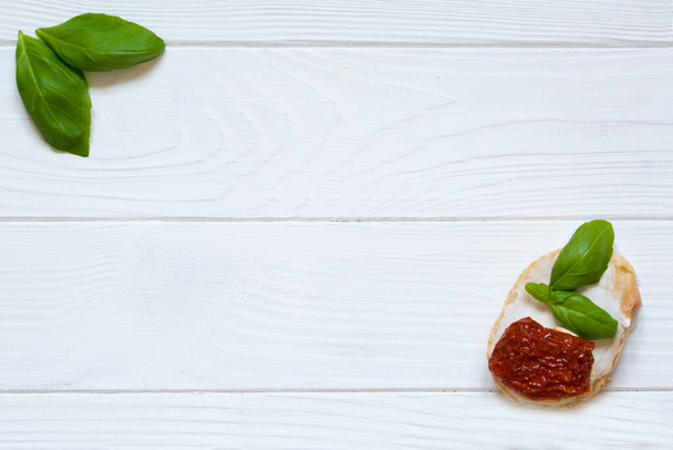 Bruschetta with dry tomatos, goat white cheese and basil on the white rustic wooden background. Italian cuisine, top view. Copy space.  - Photo, Image