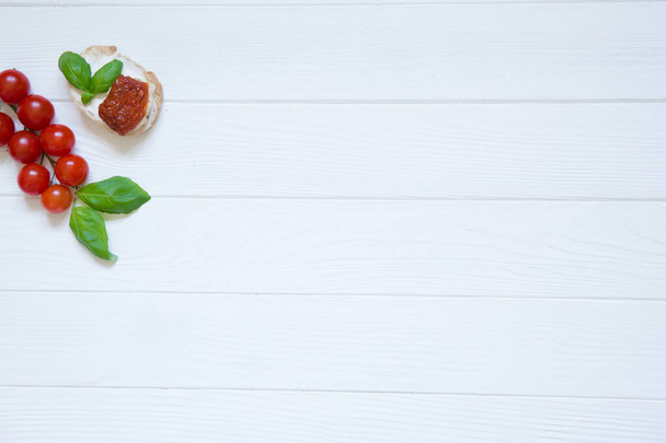 Bruschetta with dry tomatos, goat white cheese and basil on the white rustic wooden background. Italian cuisine, top view. Copy space.  - Фото, зображення