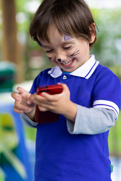 Lovely Boy with Painted Face, Playing on Mobile Phone - Foto, Imagem