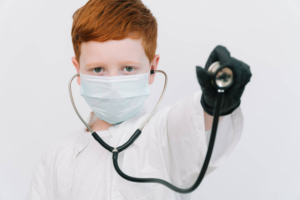 Close up of caucasian littile doctor with a stethoscope in protective mask. Reception of a patient with pneumonia covid-19 - Фото, зображення